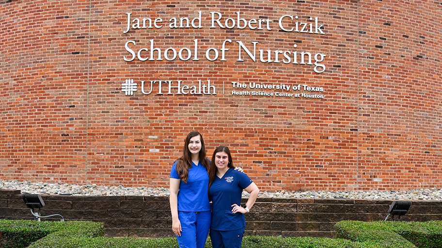 Jane Snow and Ellen Ezernack in front of a brick wall outside of Cizik School of Nursing. The text on the wall reads 