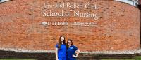 Jane Snow and Ellen Ezernack in front of a brick wall outside of Cizik School of Nursing. The text on the wall reads 