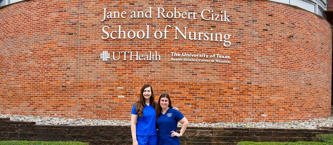 Jane Snow and Ellen Ezernack in front of a brick wall outside of Cizik School of Nursing. The text on the wall reads 